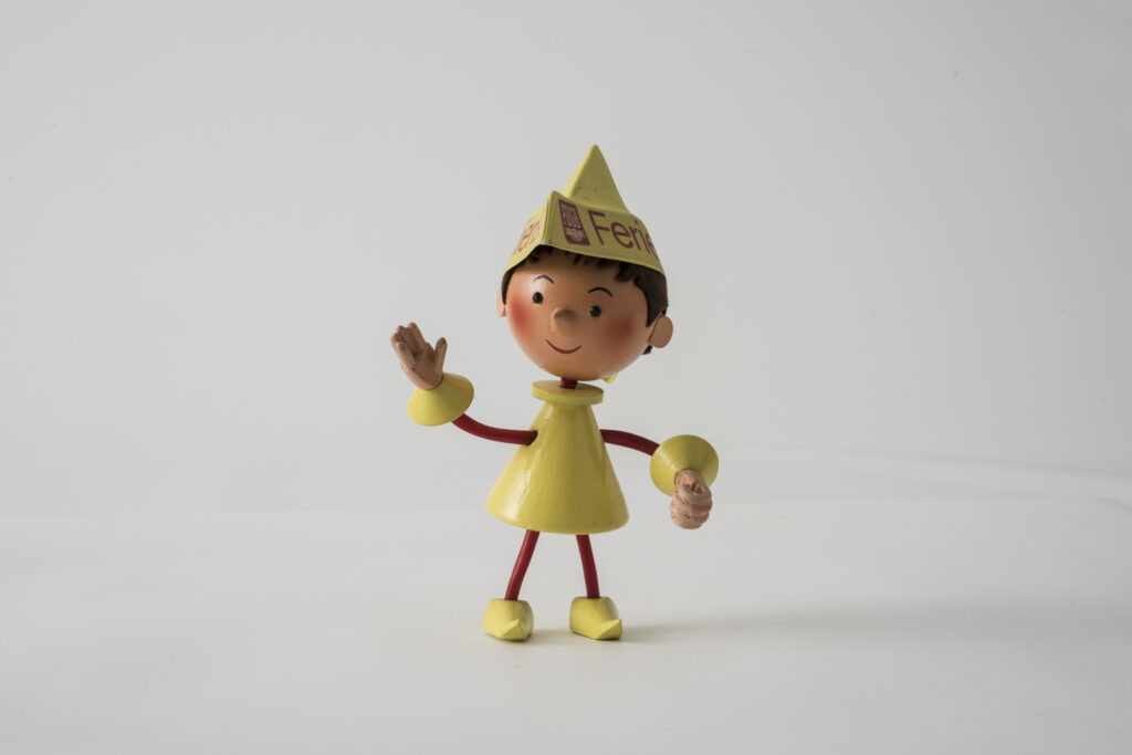 wooden puppet with bright yellow clothing and a hat with the lettering Feriendienst