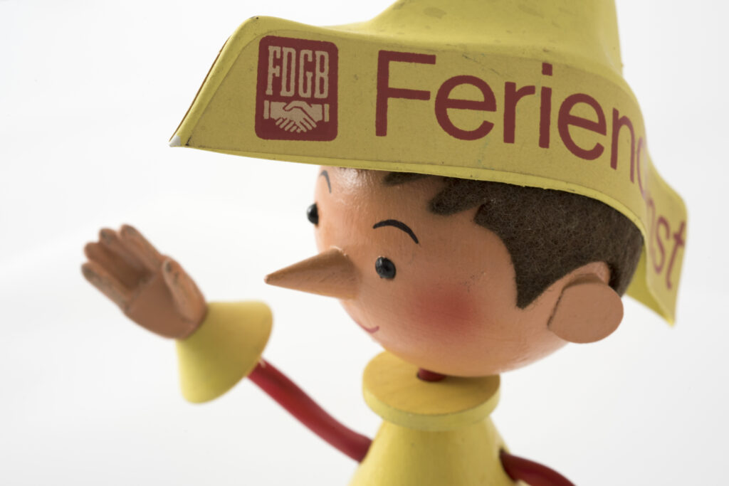 wooden puppet with bright yellow clothing and a hat with the lettering Feriendienst, detail of the head
